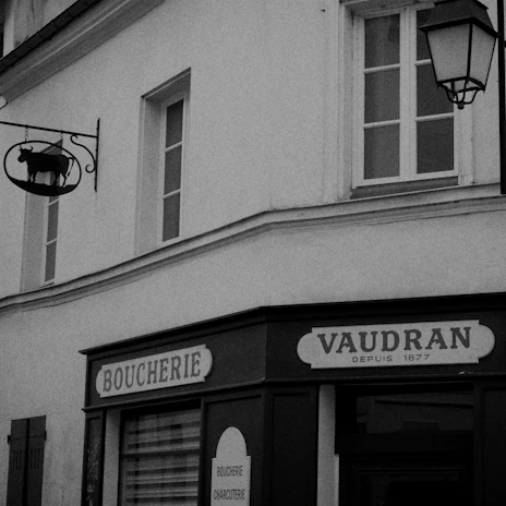 A mobile butcher van parked in a rustic village street near Bourg-en-Bresse, with elegant black and gold branding.