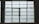 A large, rectangular window with multiple panes arranged in a grid pattern. The glass appears to be frosted or opaque, allowing minimal visibility to the outside. The window has simple metal latches for opening the panes, and there is a small green sign on the left side.