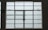 A large, rectangular window with multiple panes arranged in a grid pattern. The glass appears to be frosted or opaque, allowing minimal visibility to the outside. The window has simple metal latches for opening the panes, and there is a small green sign on the left side.