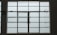 A large, rectangular window with multiple panes arranged in a grid pattern. The glass appears to be frosted or opaque, allowing minimal visibility to the outside. The window has simple metal latches for opening the panes, and there is a small green sign on the left side.