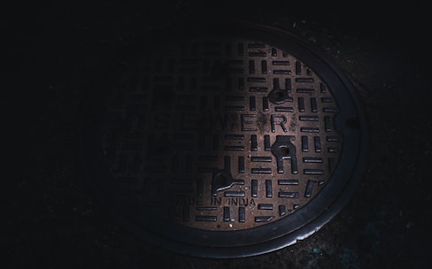 Close-up of a smart sewer monitor device mounted on a manhole cover surrounded by urban infrastructure.