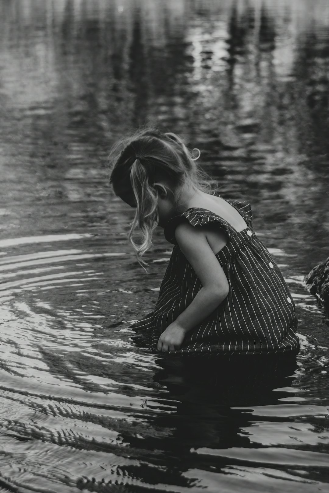 grayscale photo of woman in black and white stripe dress on water