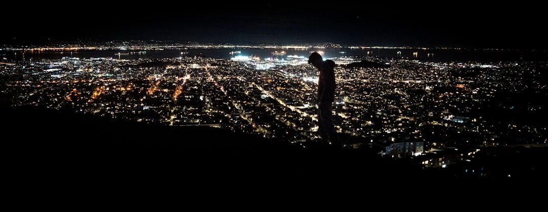 man standing on the ground looking at the city lights during night time