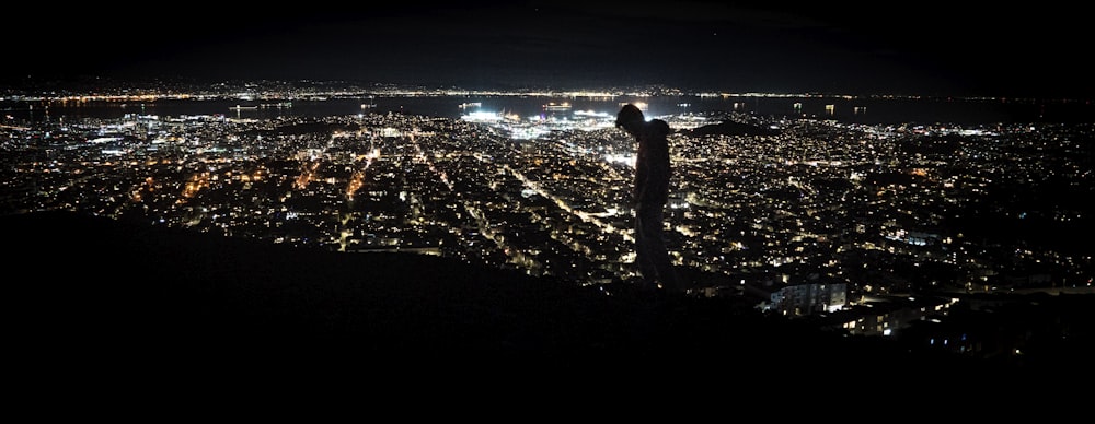 man standing on the ground looking at the city lights during night time