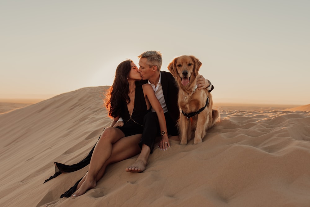 2 Frauen sitzen tagsüber auf Sand neben braunem Hund