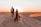 Couple walking hand in hand across golden sand dunes with a sunset backdrop
