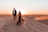 Couple walking hand in hand across golden sand dunes with a sunset backdrop
