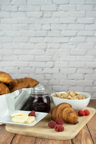 A rustic wooden board with freshly baked croissants and a jar of homemade jam