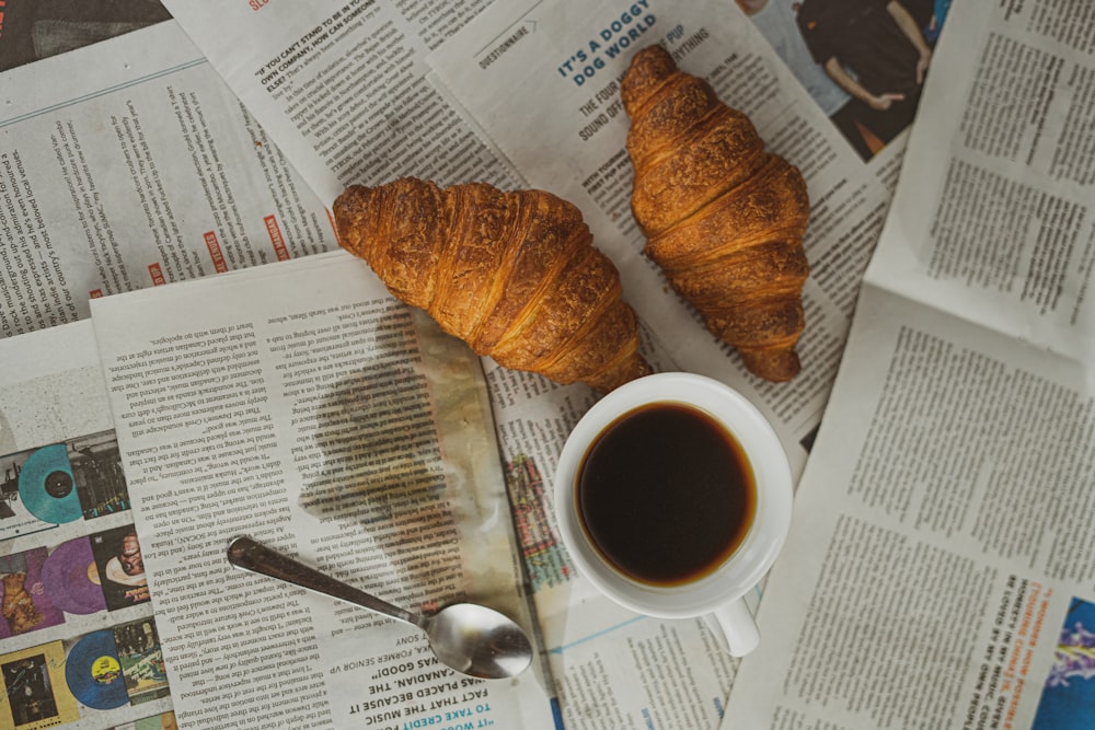 white ceramic mug with coffee beside brown bread on white paper