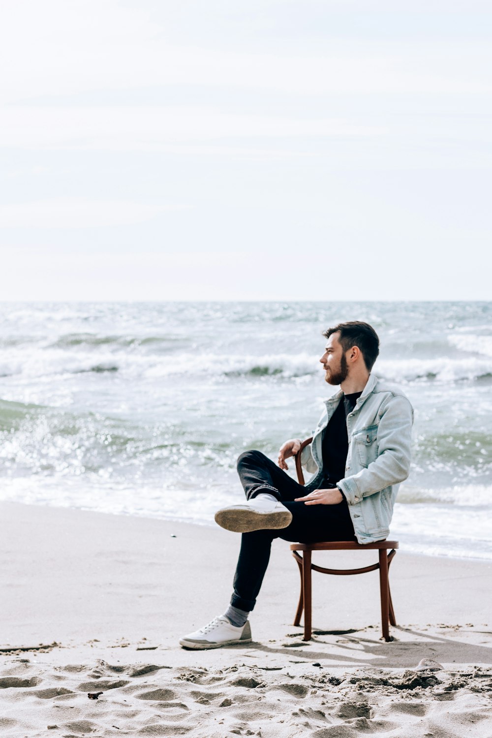 man in gray jacket sitting on brown wooden chair on beach during daytime