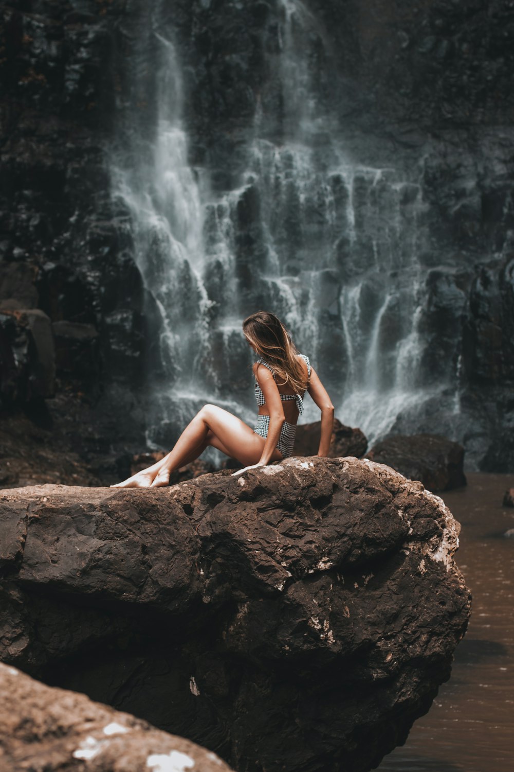 woman in black bikini sitting on brown rock near waterfalls during daytime