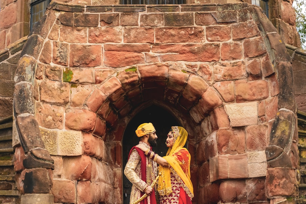 woman in yellow and red dress holding yellow umbrella standing beside brown brick wall