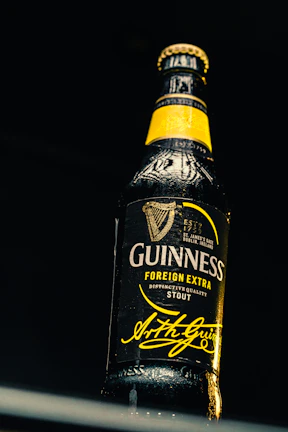 Close-up of a frosty Heller beer bottle with a guitar in the background on a dimly lit stage.
