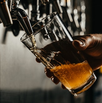 person pouring brown liquid on clear drinking glass