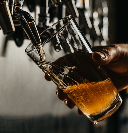 person pouring brown liquid on clear drinking glass