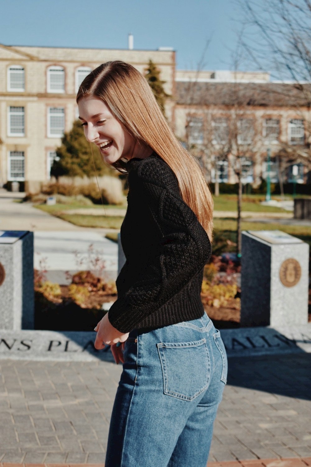 woman in black sweater and blue denim jeans standing on gray concrete floor during daytime