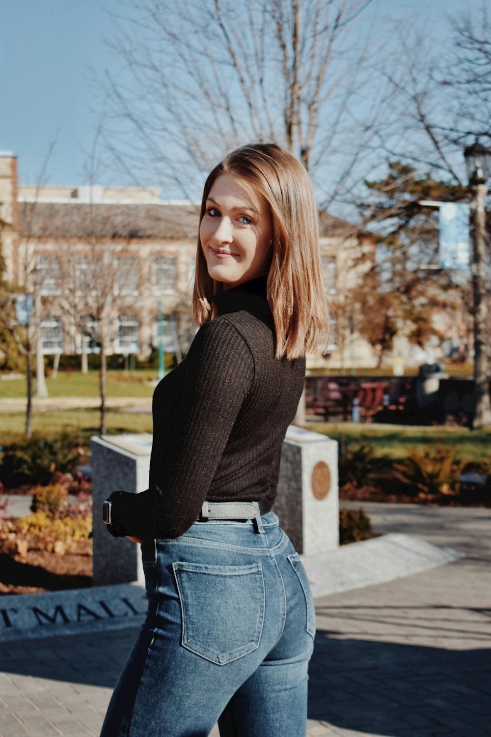 woman in brown sweater and blue denim jeans standing near trees during daytime