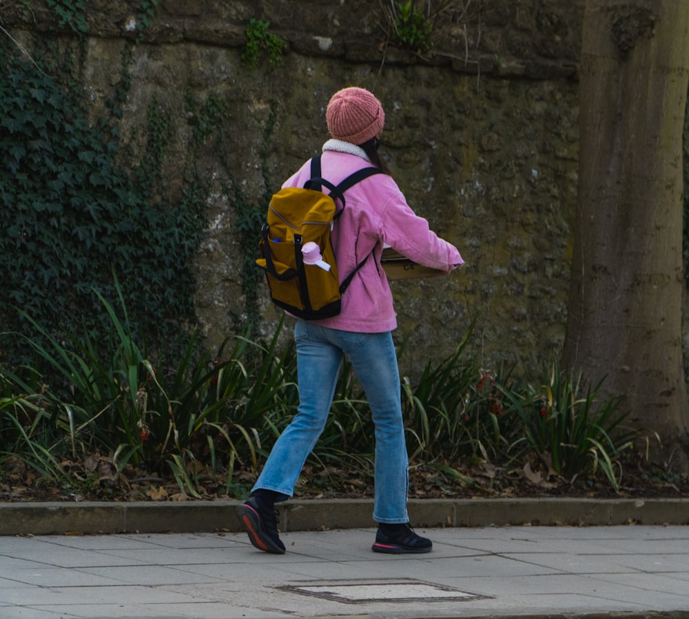 woman in pink hoodie and blue denim jeans walking on sidewalk