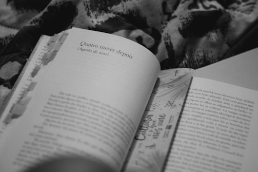 A black and white image of an open book featuring a section header titled 'Quatro meses depois (Agosto de 2011)'. The book has multiple paper tabs inserted along the top edge, and it rests on a patterned surface that appears to be a fabric.
