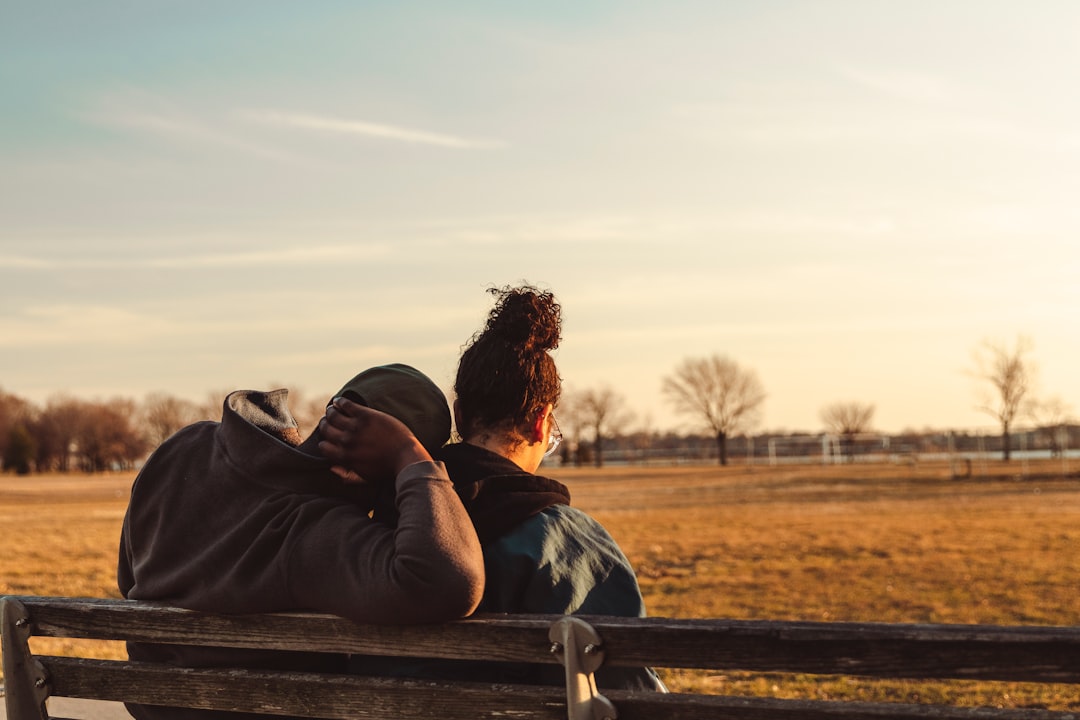 man and woman kissing on brown wooden bench during daytime