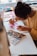 A person engrossed in painting with watercolors, using a vibrant palette and brush to create floral designs on paper. The workspace is filled with artistic tools and materials, creating a creative atmosphere.
