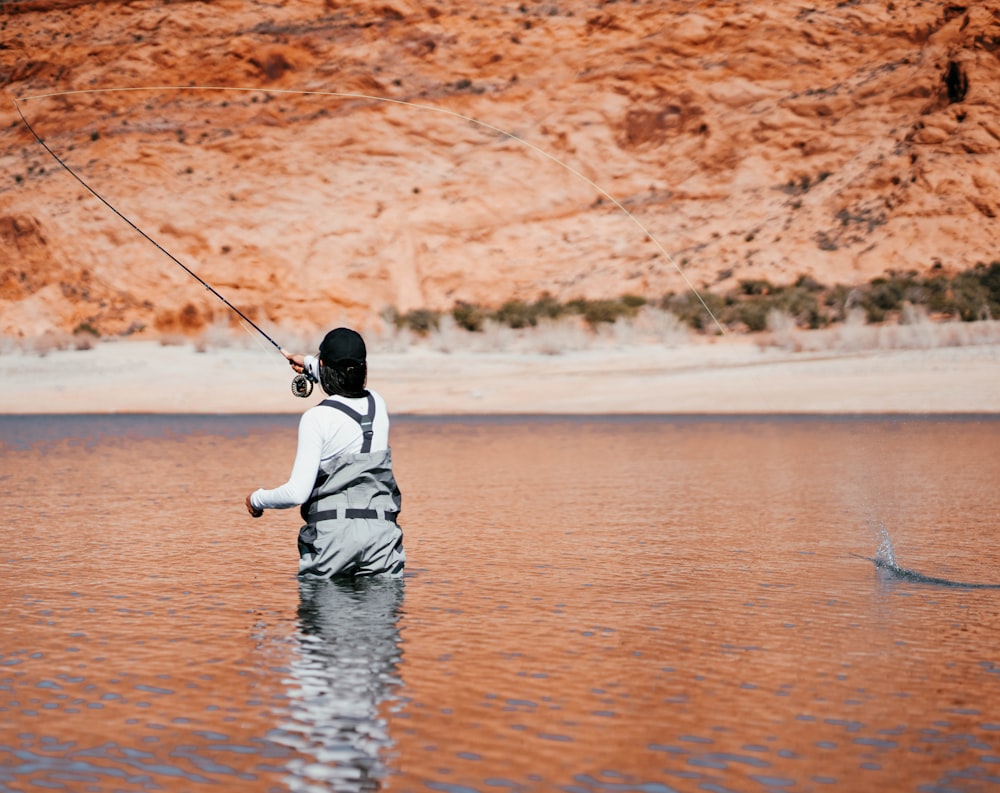 child in white hoodie and black pants fishing on water during daytime