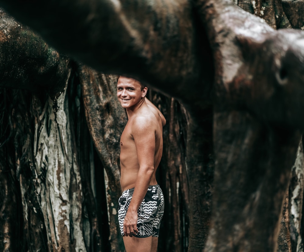 topless man in black and white shorts standing beside brown rock