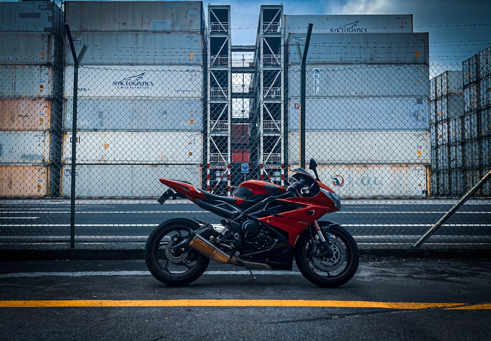 Red and black sports bike parked beside gray metal fence photo