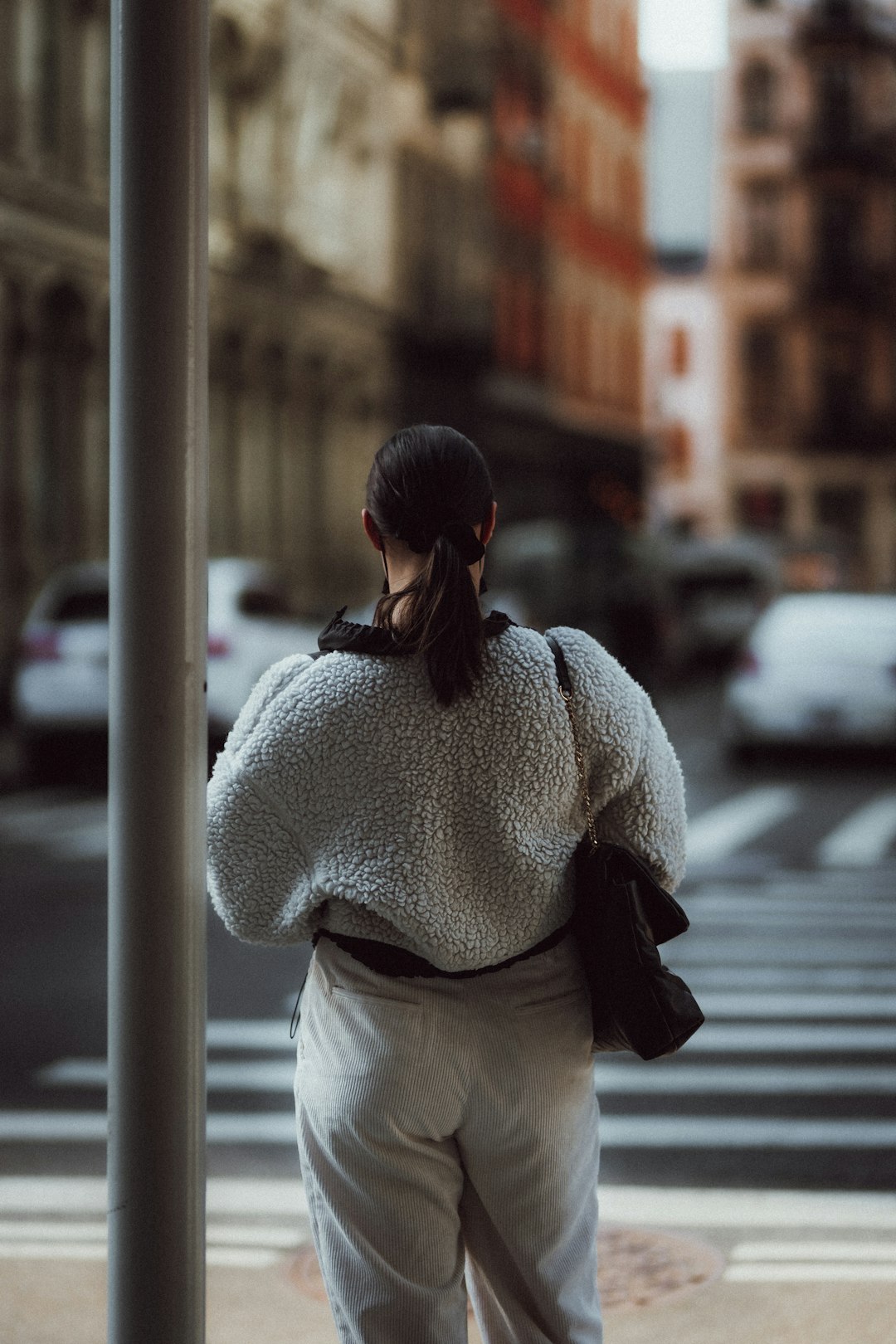 woman in white knit sweater and white skirt standing beside gray metal post during daytime