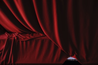 Elegant red fabric drapes in soft folds, suggesting a rich and luxurious texture. A small section of piano keys peeks through at the bottom, creating a contrast between the smooth material and the glossy, black and white keys.