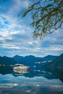 white boat on water near green mountain under white clouds and blue sky during daytime