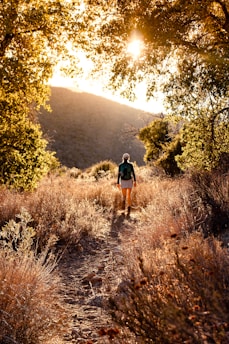 woman in black shirt and brown shorts walking on brown dirt road during daytime