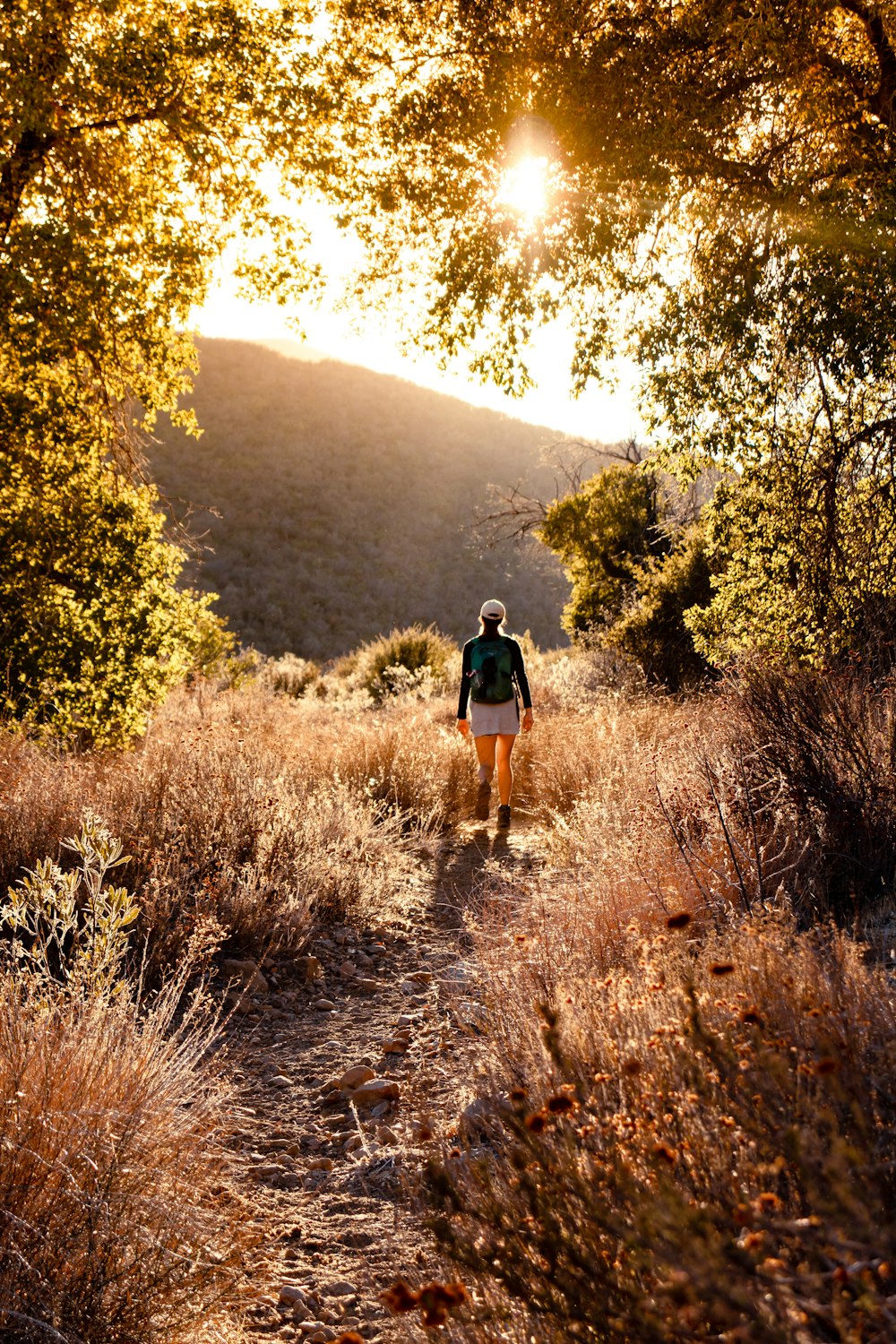 woman in black shirt and brown shorts walking on brown dirt road during daytime