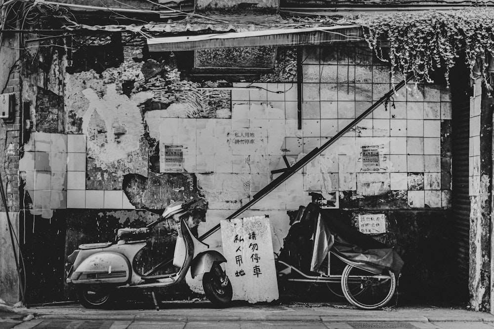 grayscale photo of motorcycle parked beside wall with graffiti