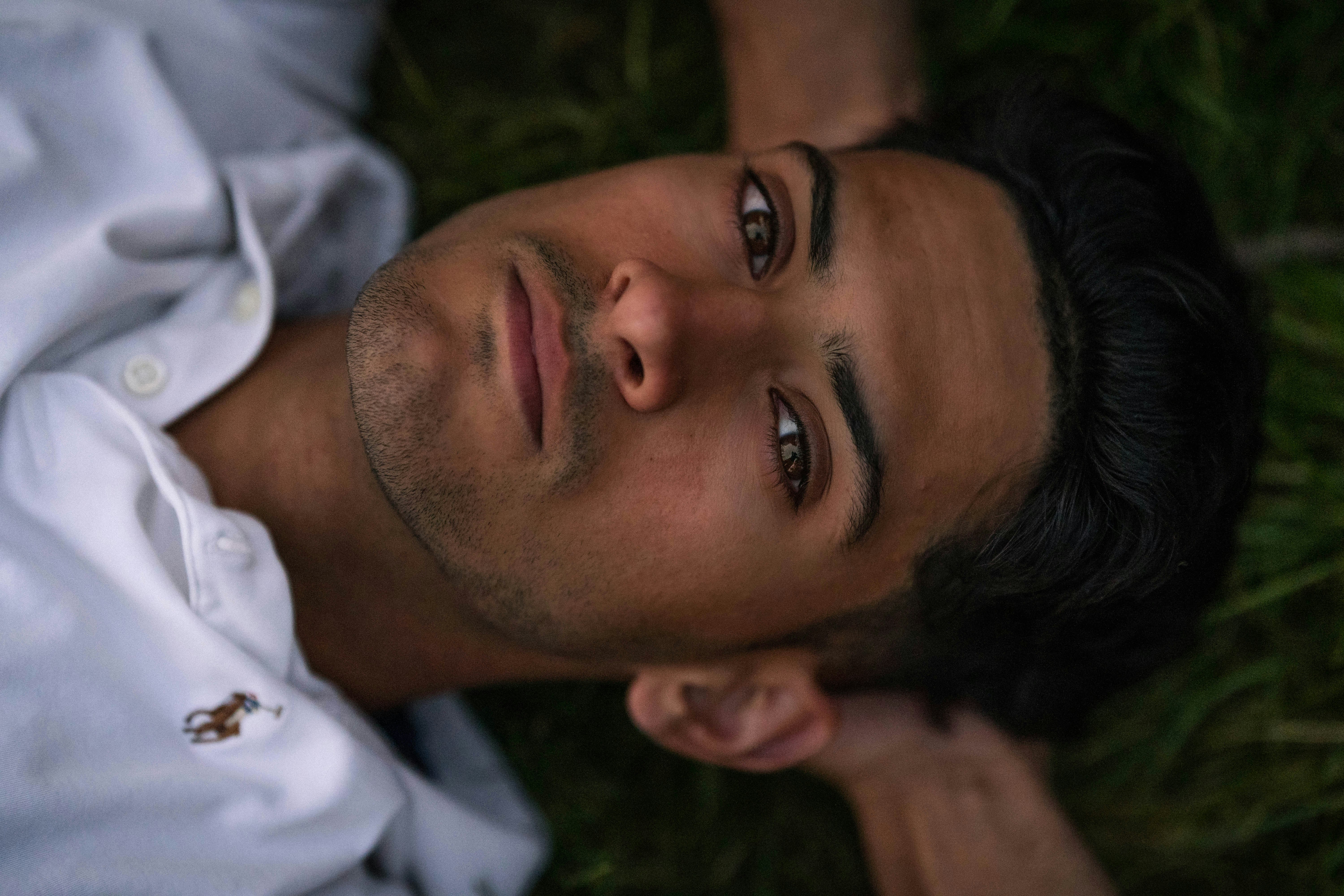 man in white button up shirt lying on green grass during daytime