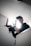 A person is holding a professional video camera, possibly in the process of filming. The light source behind them creates a halo effect around their head, casting a dramatic silhouette. The setting appears to be indoors with plain white walls.