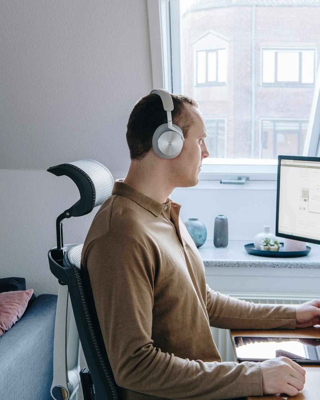 man in brown long sleeve shirt wearing white headphones sitting on black office rolling chair