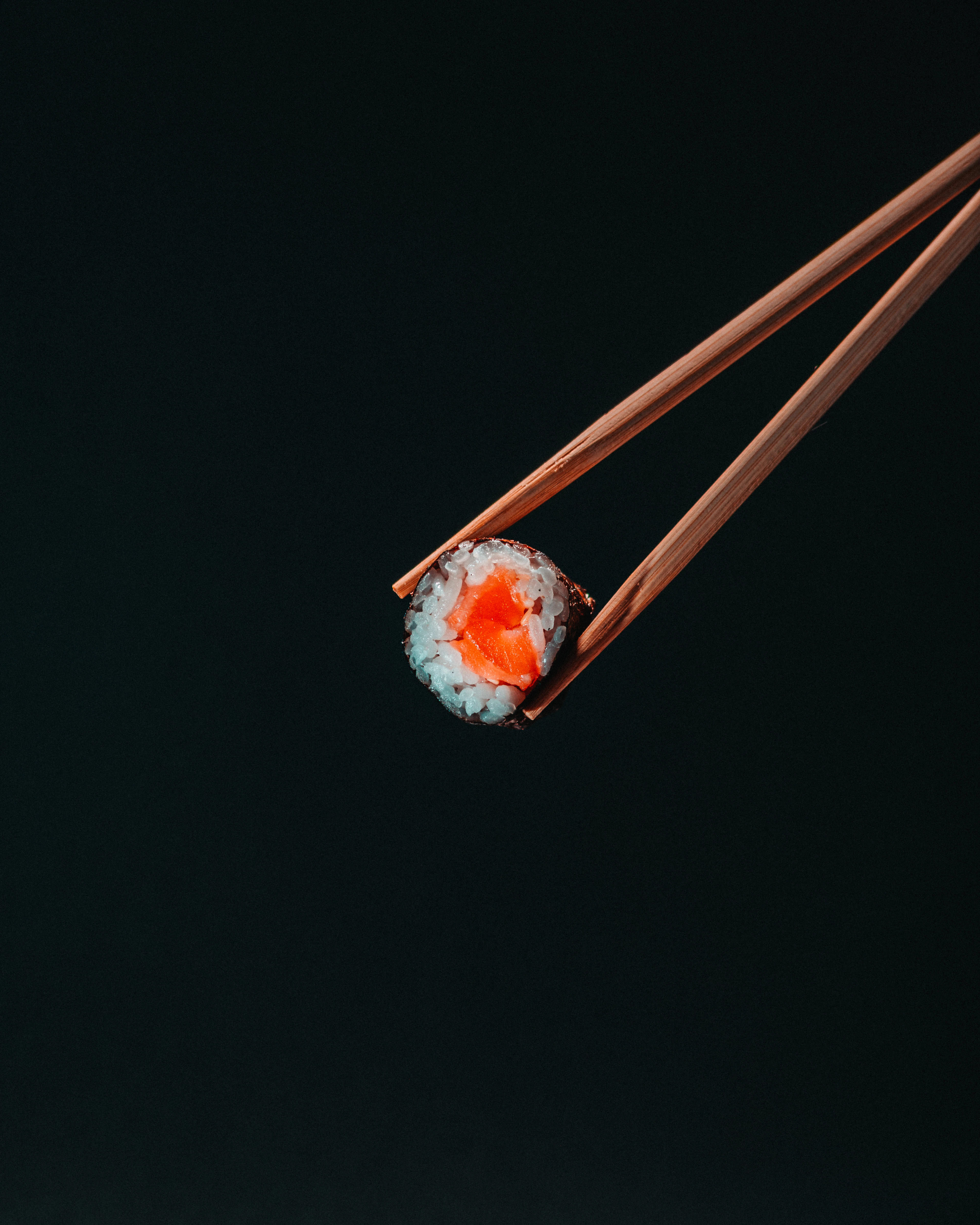A single maki piece lifted with chopsticks