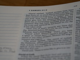 A close-up view of an open book showing a passage from 1 Samuel 21:5 in clear, bolded text. The book is slightly tilted, and the focus is on the top left section of the page, showcasing some underlined and annotated sections in the margins. The page is mostly filled with text in a traditional serif font.