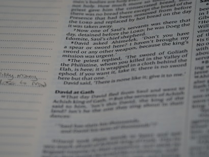 A close-up view of an open book showing text in black font on off-white pages. The text appears to be a narrative or scripture. The left page contains bullet points and some handwritten notes with a small doodle at the bottom of the page. The focus is on the right page, which contains paragraphs of printed text.