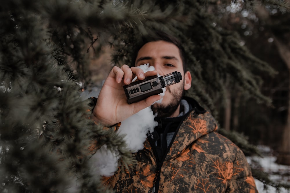 man in brown and black camouflage jacket holding black and silver camera