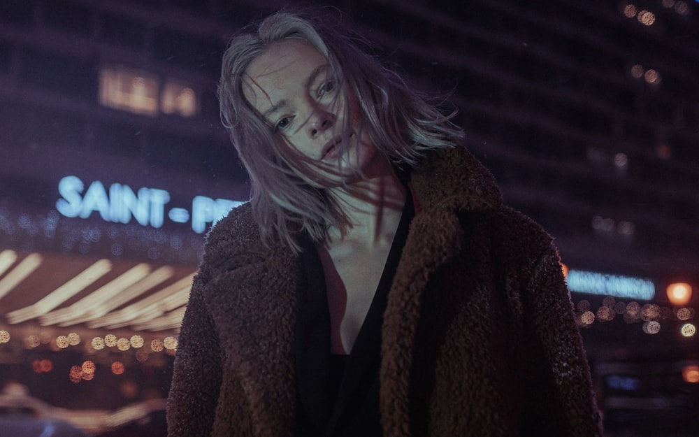 woman in brown coat standing near building during night time