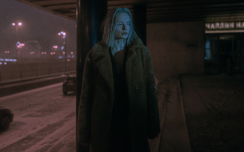 woman in black coat standing on sidewalk during night time