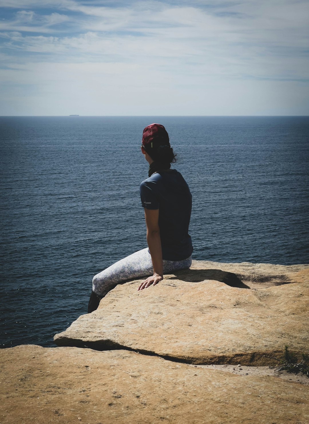 woman in black shirt sitting on brown rock formation near body of water during daytime