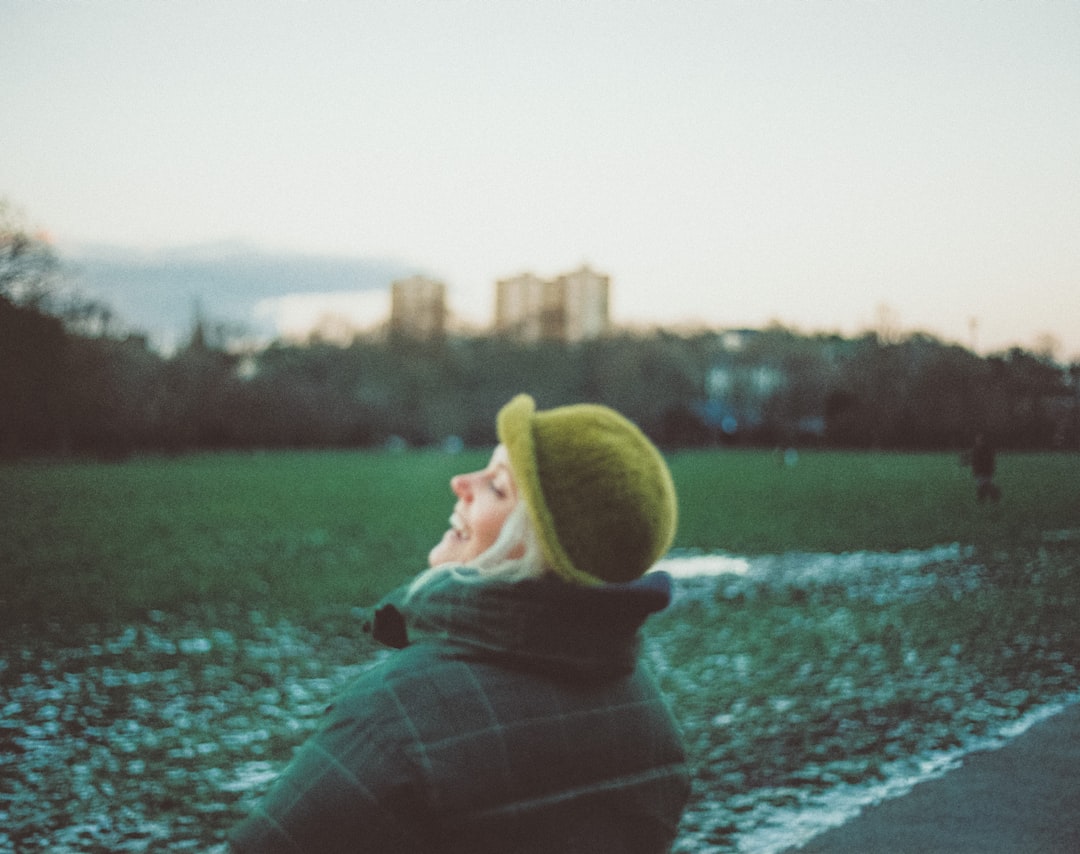 person in green and black plaid hoodie sitting on concrete pavement during daytime