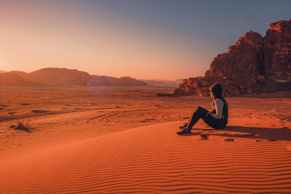 man in black shirt sitting on brown sand during daytime