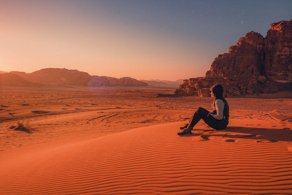 Mann im schwarzen Hemd sitzt tagsüber auf braunem Sand
