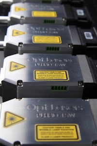 A row of metallic laser modules with visible warning labels and engraved text. The modules are aligned neatly, showcasing their industrial design. The labels contain laser hazard warnings and technical specifications.