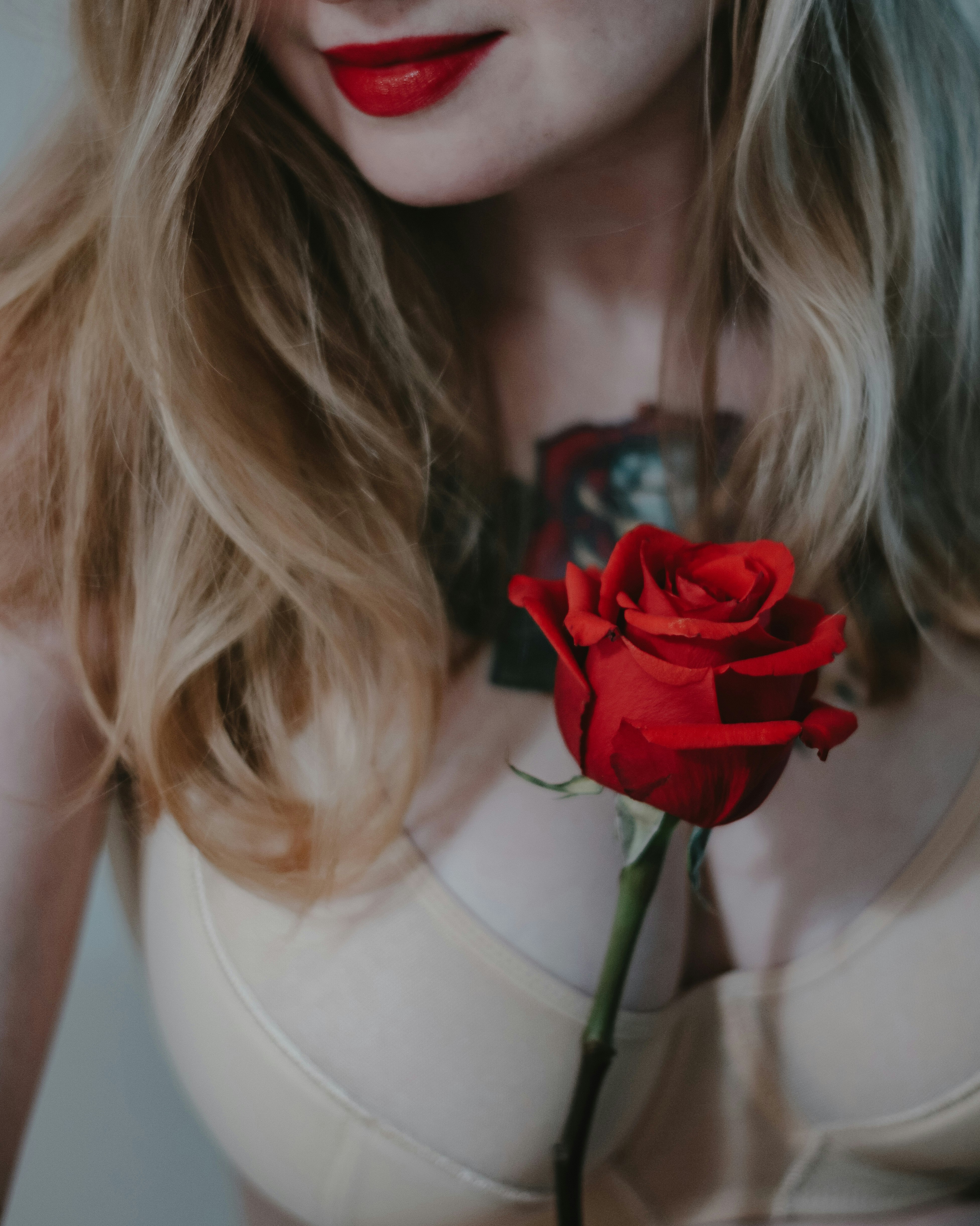 woman in white tank top holding red rose