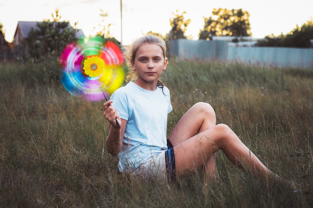 chica en camiseta blanca sin mangas y pantalones cortos azules sentada en el campo de hierba verde sosteniendo azul y